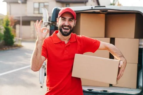 Image of a delivery man standing with parcel box and showing ok sign 스톡 사진