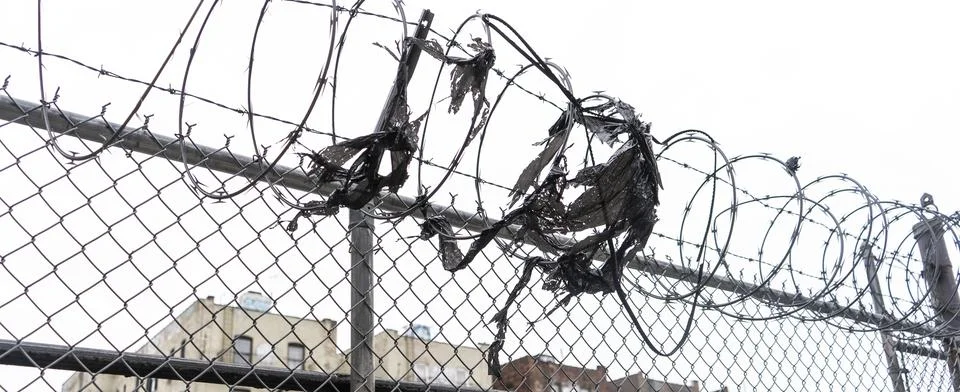 The image depicts a section of a chain link fence topped with razor wire. The Stock Photos