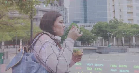 Image of diagrams and data processing over caucasian woman walking and eating in Stockfoto's