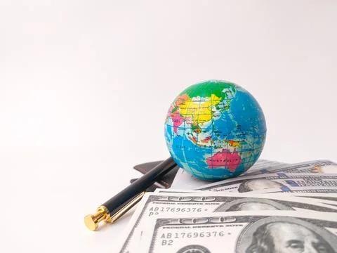 The image displays a small globe and a pen resting on top of a stack of U.S.. Stock Photos