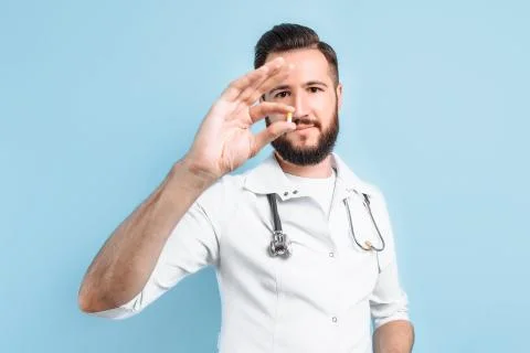 Image of a doctor's hand showing a single capsule on a light blue background Stock Photos