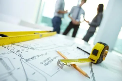 Image of engineering objects on workplace with three architects interacting on b Stock Photos