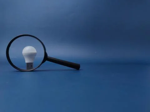 This image features a light bulb positioned on top of a magnifying glass ag.. 库存照片