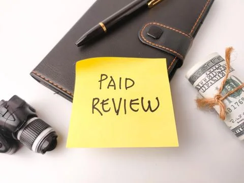 The image features a yellow sticky note with the words PAID REVIEW written .. Stock Photos