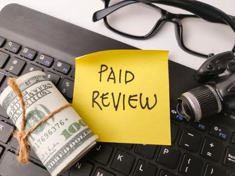 The image features a yellow sticky note with the words PAID REVIEW written .. Stock Photos