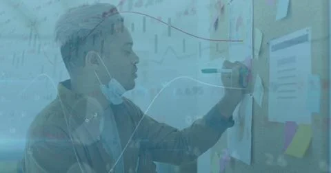 Image of financial data processing over man with face mask writing on memo note Stock Photos