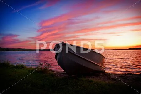 Image of fishing boat on shore of lake at sunset Stock Photos