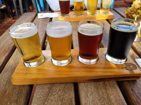 Image of four samplers of various types of beer on a wooden base and table Stock Photos