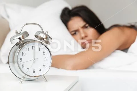 Image of frustrated woman 20s lying in bed on pillow, and looking on ringing Stock Photos