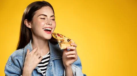 Image of girl smiling while biting slice of pizza, happy face at pizzeria Stock Photos