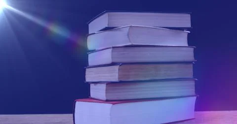 Image of glowing light over stack of books on blue background Stock Photos