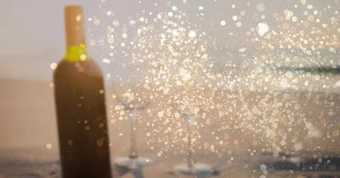 Image of gold dots over blurred bottle of red wine on beach Ilustração Stock