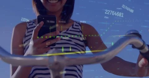 Image of graph and processing data over caucasian woman on bike using smartphone Stock Photos