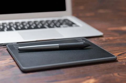 Image of a graphics tablet, stylus and laptop on a wooden table. Designer w.. Stock Photos