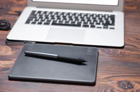 Image of a graphics tablet, stylus and laptop on a wooden table. Designer w.. Stock Photos
