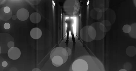 Image of grey bokeh light spots over scary figure backlit in doorway at end of Stock-Fotos