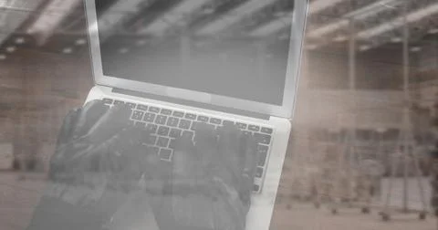 Image of hacker in gloves using laptop with stacks of boxes in warehouse Stock-Fotos