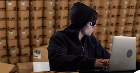 Image of hacker using laptop with stacks of boxes in warehouse Stock Photos