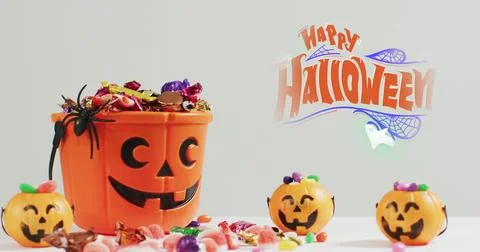 Image of halloween text over carved pumpkin bucket with sweets on grey Fotos Stock