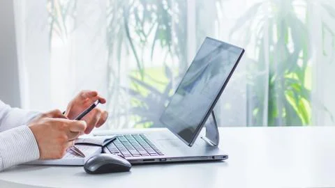 An image of the hands of a man sitting at a table and writing in a Notepad wi Foto stock