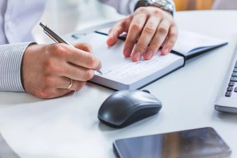 An image of the hands of a man sitting at a table and writing in a Notepad wi Stock Photos