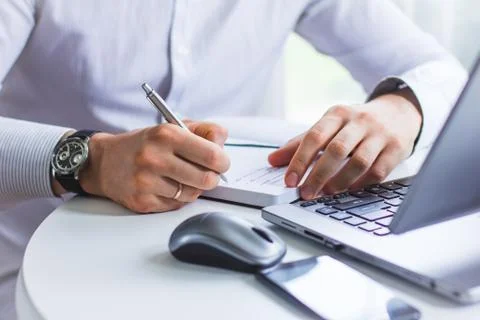 An image of the hands of a man sitting at a table and writing in a Notepad wi Stock Photos