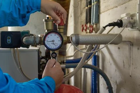 Image of the hands of a plumber who opens a hot water tap of a boiler. Stock Photos