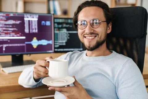 Image of handsome joyful programmer man smiling and drinking coffee Stock Photos