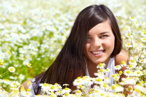 Image of happy female peeking out of chamomile glade and smiling at camera Stock Photos