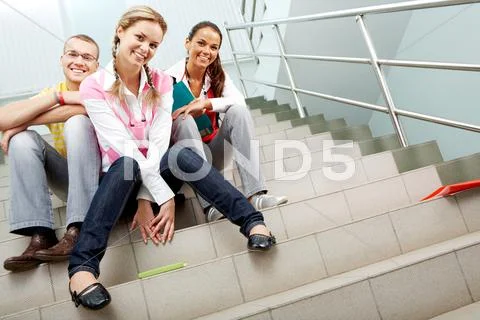 Image of happy teenagers sitting in the corridor of college and looking at camer Stock Photos