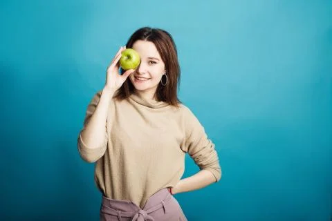 Image of a happy young girl standing on a blue background holding a green apple Stock Photos
