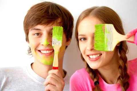 Image of joyful couple hiding one of eyes behind paintbrushes with green color Stock Photos