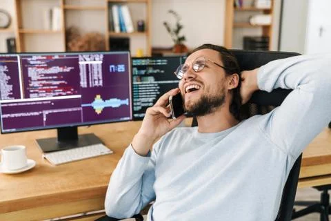 Image of joyful programmer man laughing and talking on cellphone Stock Photos
