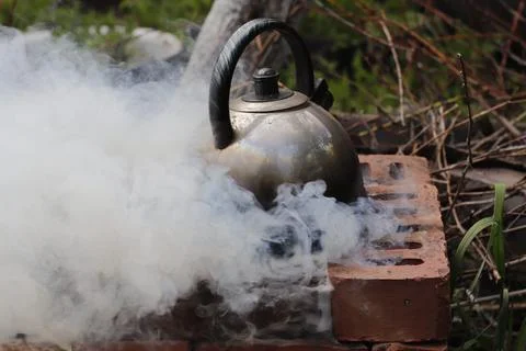 An image of a kettle on a makeshift open-air stove, shrouded in thick smoke. Stock Photos