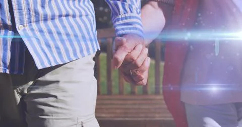 Image of light moving over midsection of senior couple walking in park holding Fotos Stock
