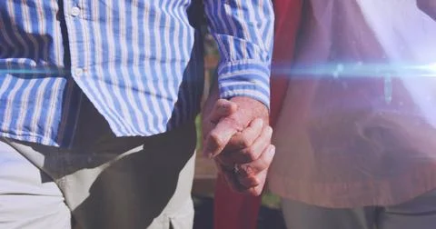 Image of light moving over midsection of senior couple walking in park holding Fotos Stock