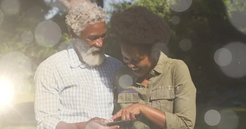 Image of light spots over african american couple using smartphone Ilustração Stock