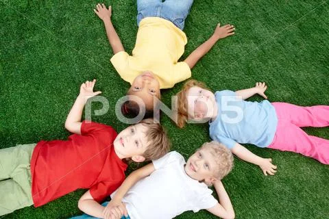 Image of little boys and girls lying on green grass and looking up Stock Photos