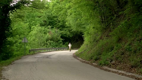 Image of a man jogging alone at calm road surrounded by forest, Croatia. Stock Footage 132726180