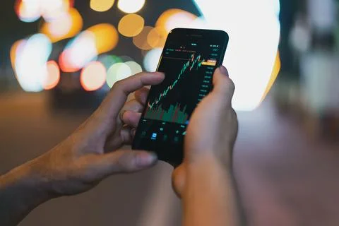 Image of a man's hand using his phone to check the stock exchange Stock Photos