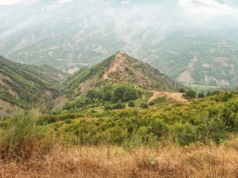 An image of mountains and fields with clouds coming from them Stock Photos