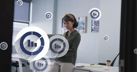 Image of multiple bar graph icons floating over asian woman using laptop at Stock Photos