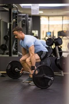 Image of a muscular man pulling a heavy barbell at the gym. Stock Photos