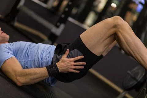 Image of a muscular man using a bench to make abdominal exercise at the gym. Stock Photos
