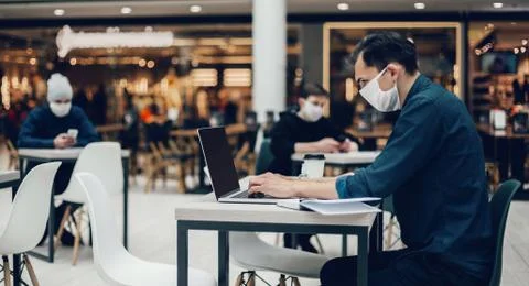 Image of people in protective masks using laptops in a food court. Stock Photos