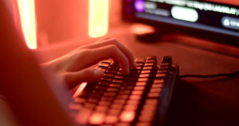 Image person keyboard with blue screen dark room, suggesting tech work coding Video stock 280130194