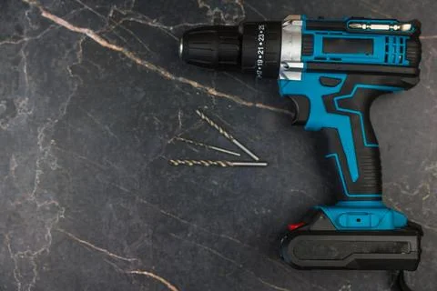 An image of a power drill placed on a dark surface alongside some screws for Stock-Fotos