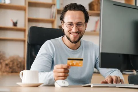 Image of programmer man holding credit card while working with computer Stock Photos