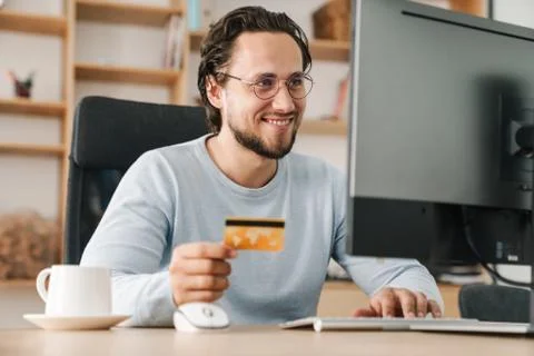 Image of programmer man holding credit card while working with computer Stock Photos