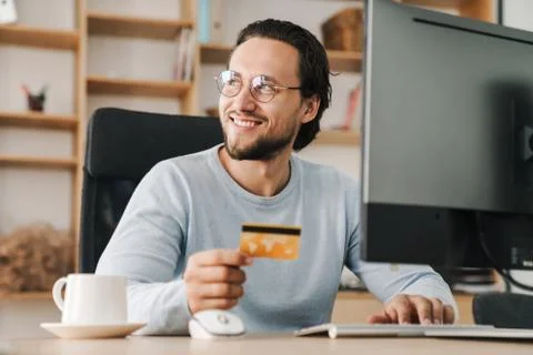 Image of programmer man holding credit card while working with computer Stock Photos